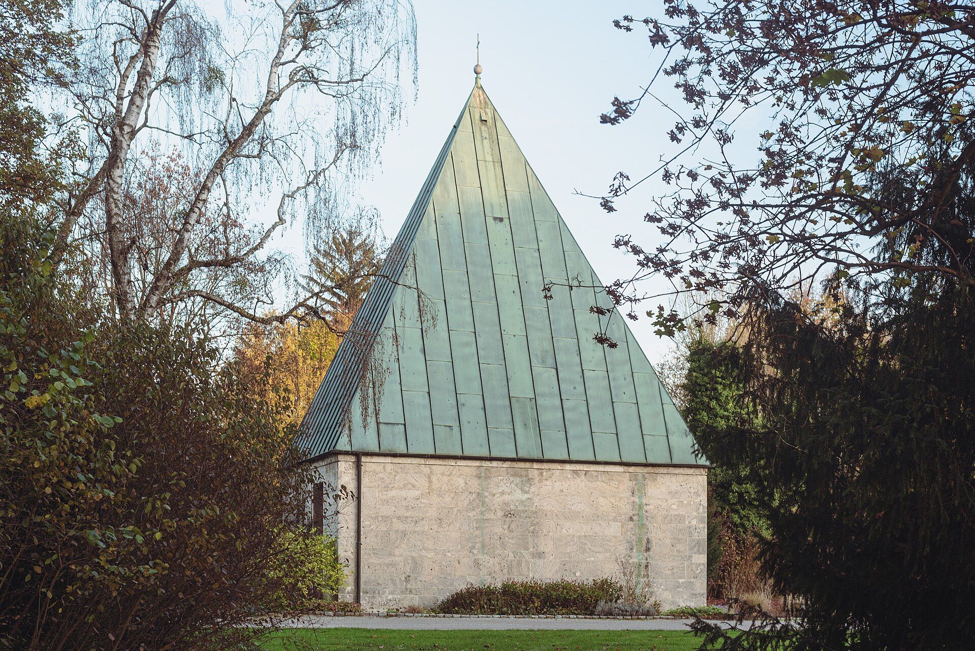 Urnenhalle am Teich mit steilem grünem Dach zwischen Bäumen auf dem Westfriedhof München
